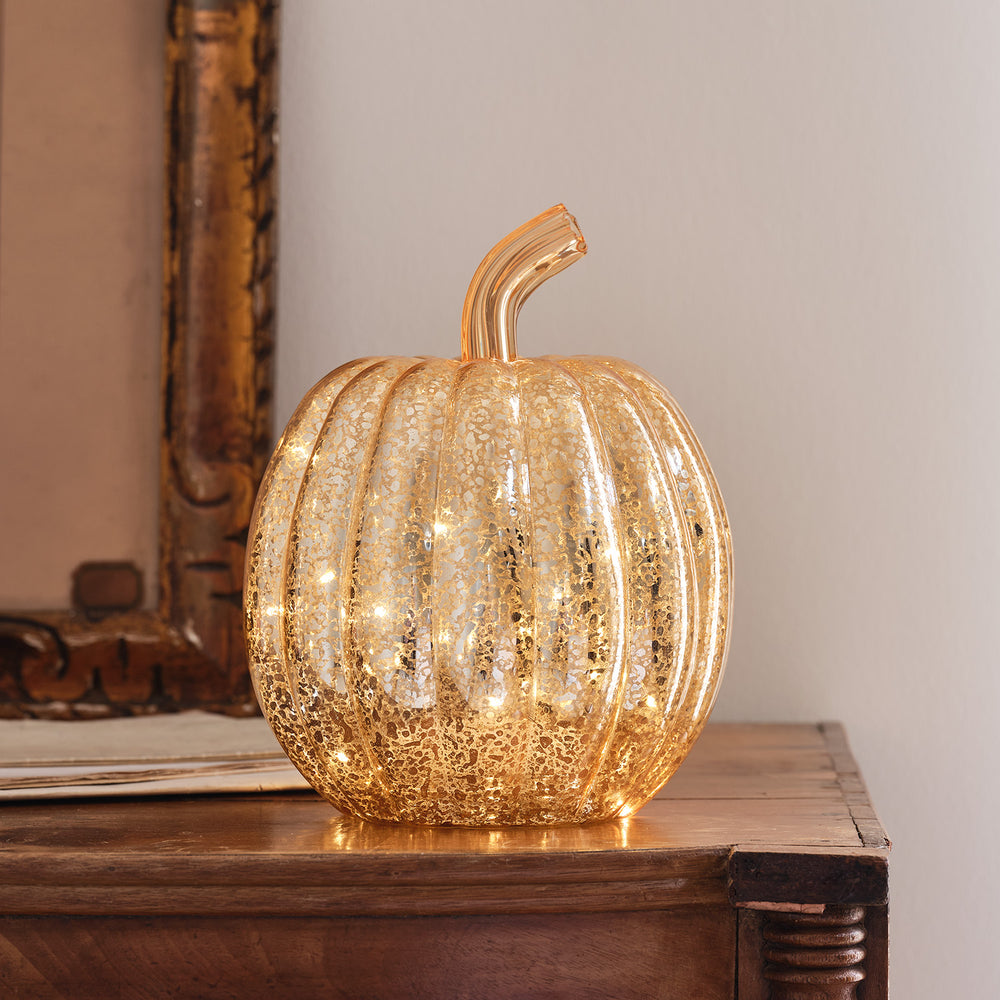 Antikgoldener LED Deko Kürbis aus Glas mit leuchtenden Lichtern auf Holztisch vor Wand