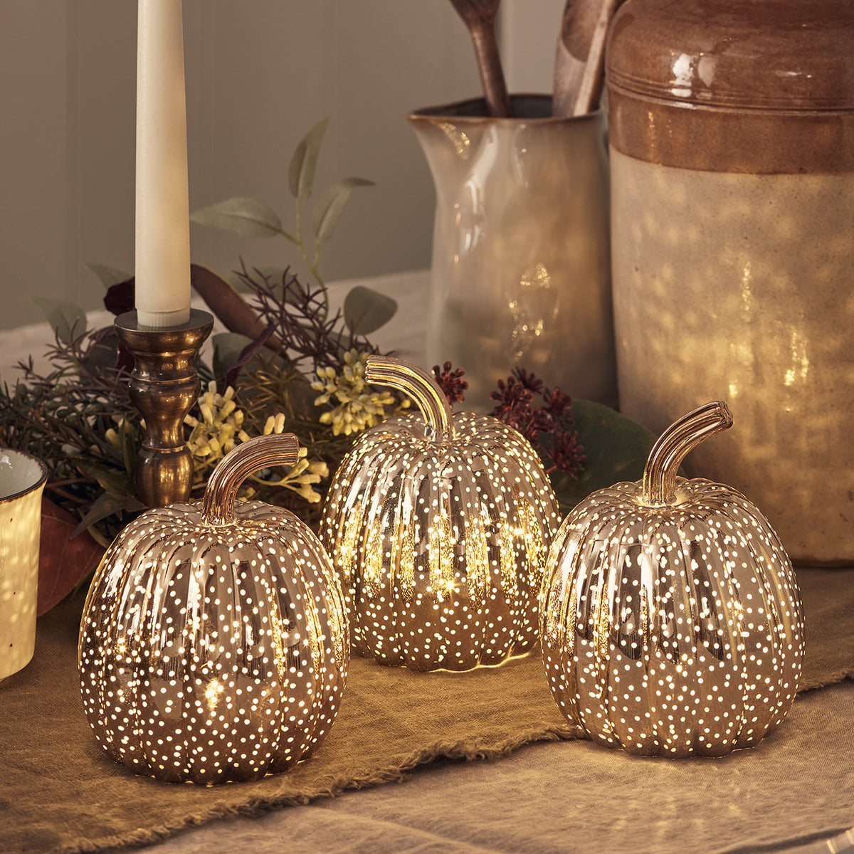 Beleuchtete Mini-LED-Kürbisse aus Glas mit Herbstdeko und Kerze im Hintergrund
