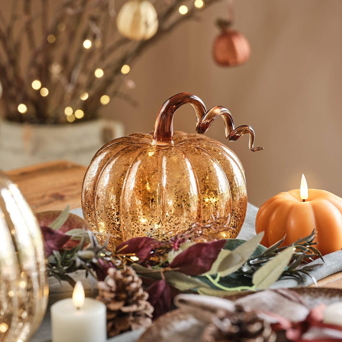 Leuchtender bernsteinfarbener LED-Kürbis mit gewelltem Stiel auf gedecktem Tisch mit Herbstdeko