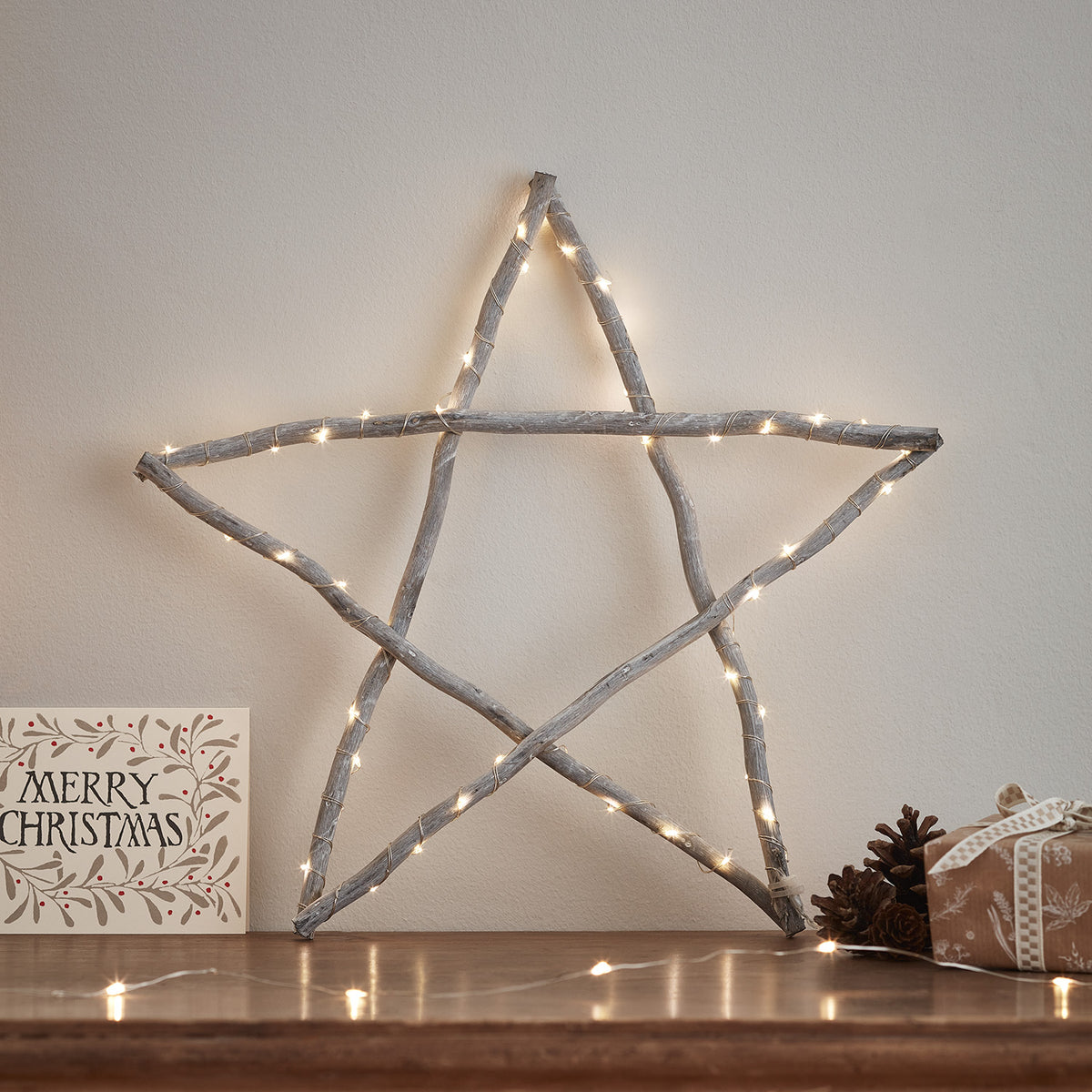 Beleuchteter Holzstern mit warmweißen LEDs vor heller Wand mit Weihnachtskarte und Tannenzapfen