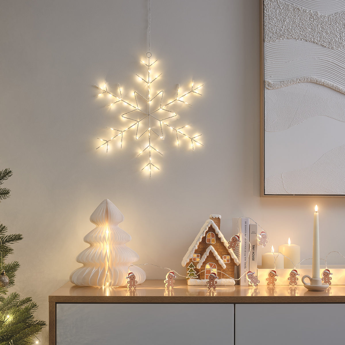 LED-Schneeflocke an Wand über Sideboard mit Weihnachtsdeko und Kerzen