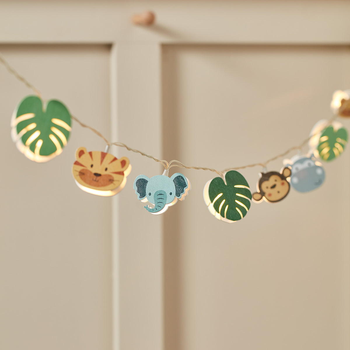Lichterkette mit Holzfiguren Tiger, Elefant, Affe und grünen Blättern an hellem Hintergrund