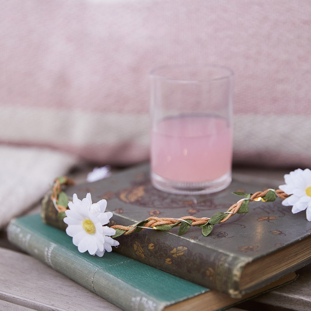 LED-Gänseblümchen-Girlande liegt auf zwei alten Büchern mit Glas rosa Getränk und rosa Stoff im Hintergrund