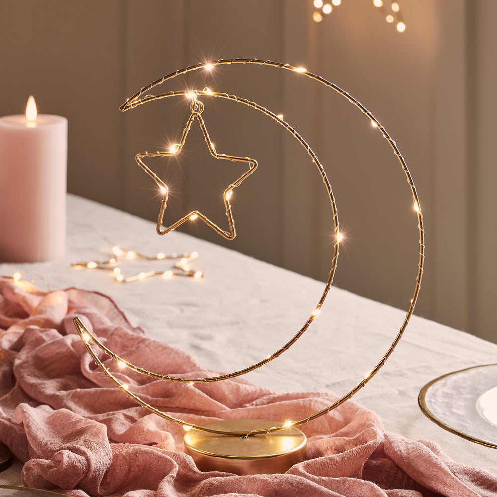 Goldfarbene Mond-Tischleuchte mit LED-Lichterkette und Stern auf einem Tisch mit rosa Tuch