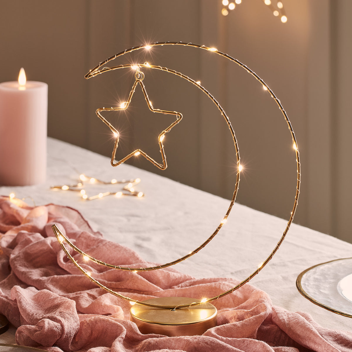 Goldfarbene Mond-Tischleuchte mit LED-Lichterkette und Stern auf einem Tisch mit rosa Tuch
