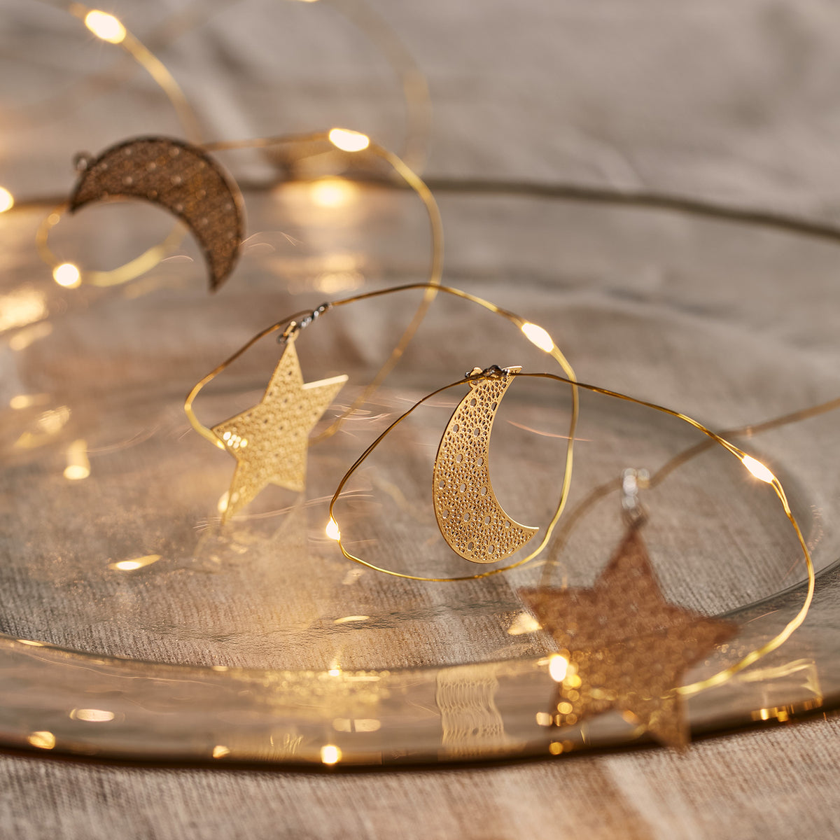 Goldene Micro Lichterkette mit filigranen Mond- und Sternanhängern auf hellem Untergrund