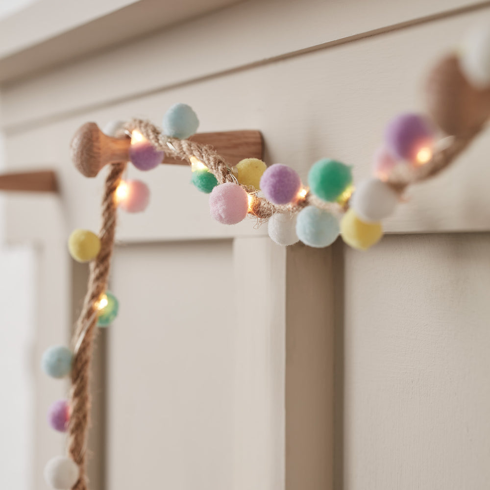 Nahaufnahme der LED-Girlande mit bunten Pompons an einem Holzknauf