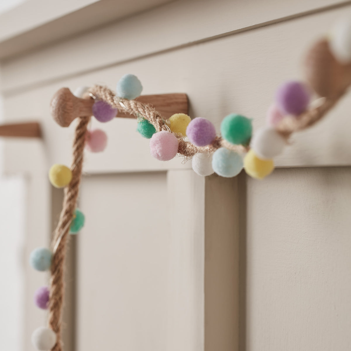 Detailaufnahme der LED-Girlande mit bunten Pompons an einem Holzknauf