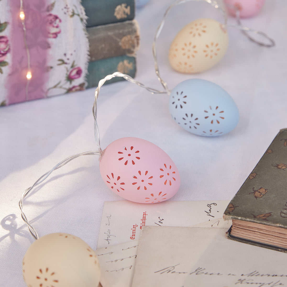Nahaufnahme der Lichterkette mit bunten Ostereiern auf weißem Tisch mit Büchern und Briefen