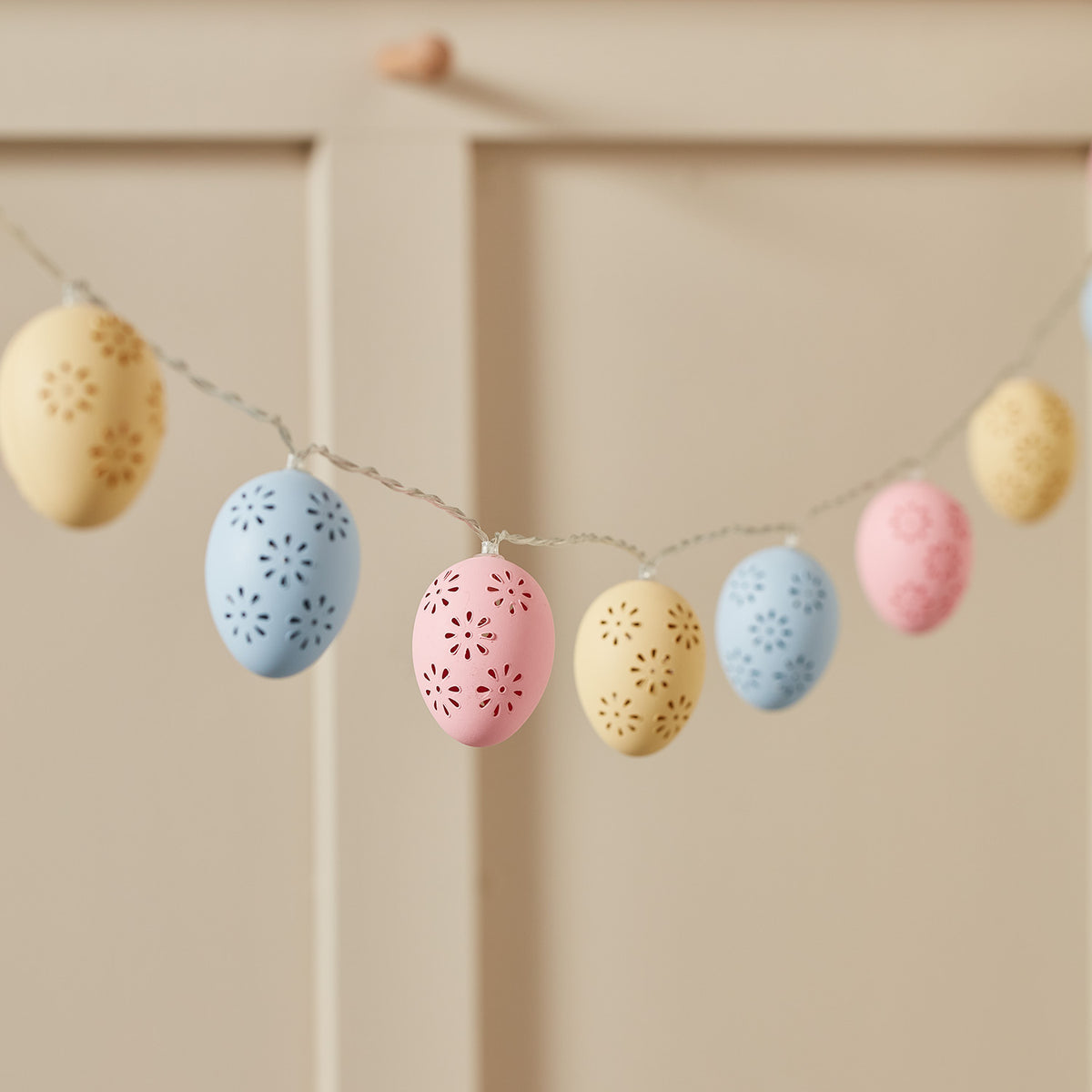 Pastellfarbene Ostereier-Lichterkette mit Blumenmuster an einer Wand hängend