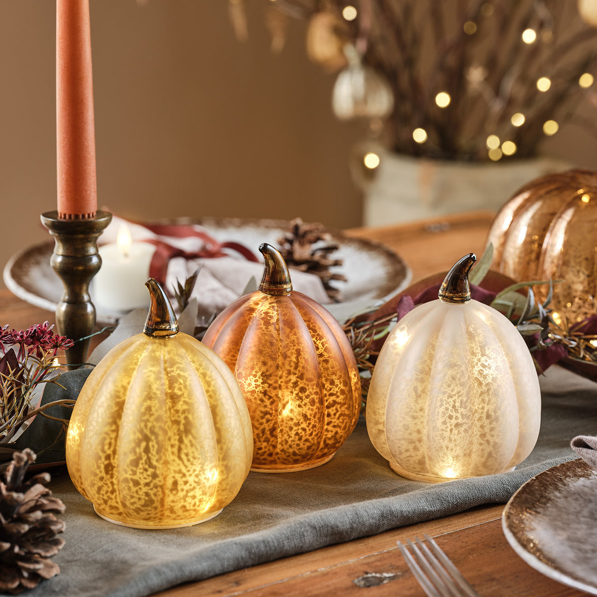 Herbstliche Dekoration mit leuchtenden Glas Kürbissen auf Kommode