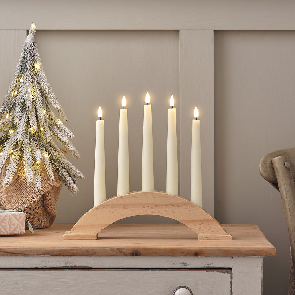 Holz-Kerzenbrücke mit fünf beleuchteten LED-Stabkerzen auf einem Tisch neben einem kleinen Weihnachtsbaum