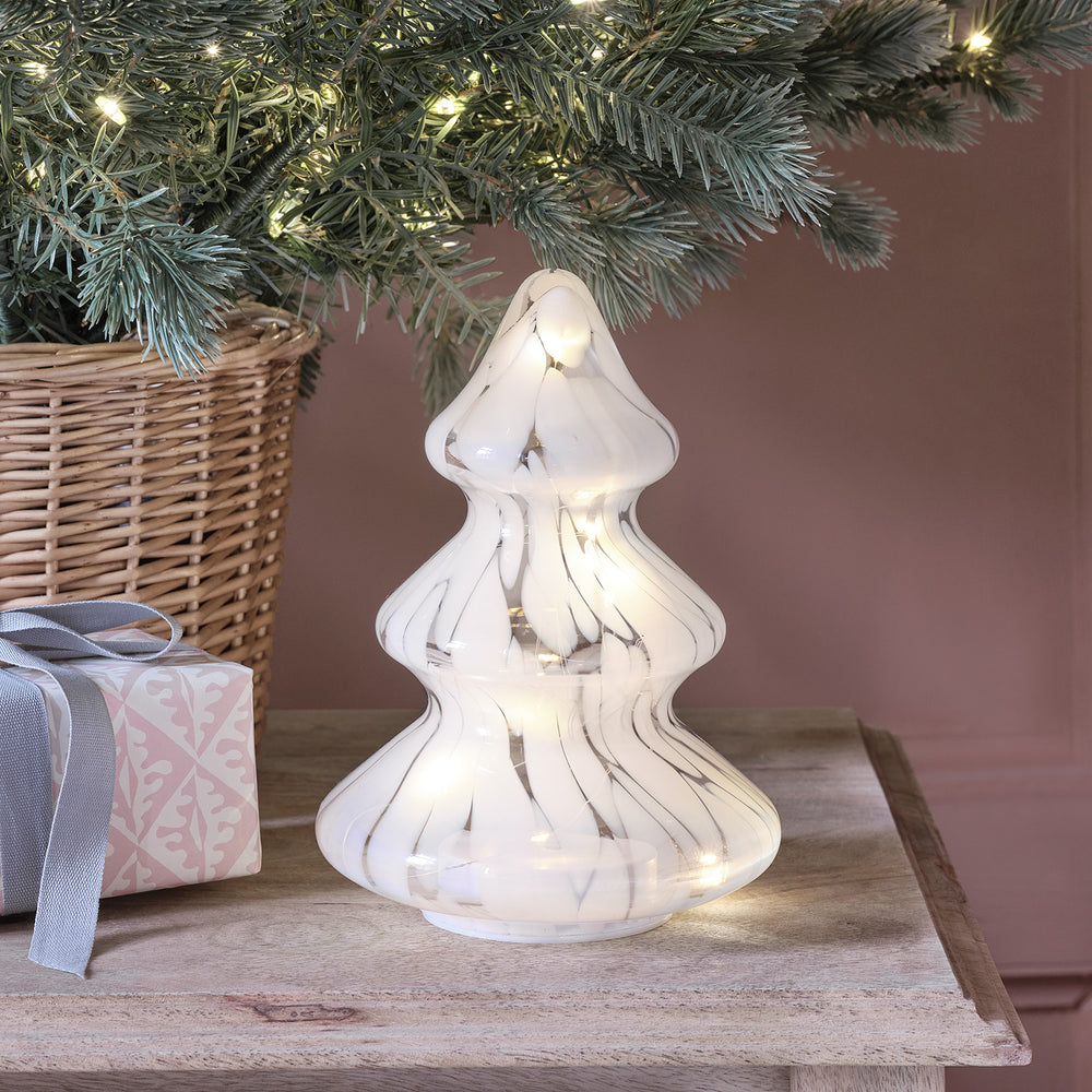 Weiß gefleckter LED Glas Tannenbaum mit Micro Lichterkette auf Holztisch neben Korb und Geschenk