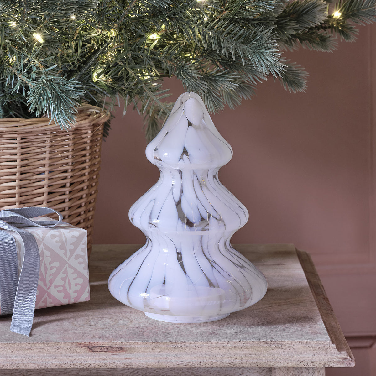 Nahaufnahme weiß gefleckter LED Glas Tannenbaum mit warmem Licht auf Holztisch