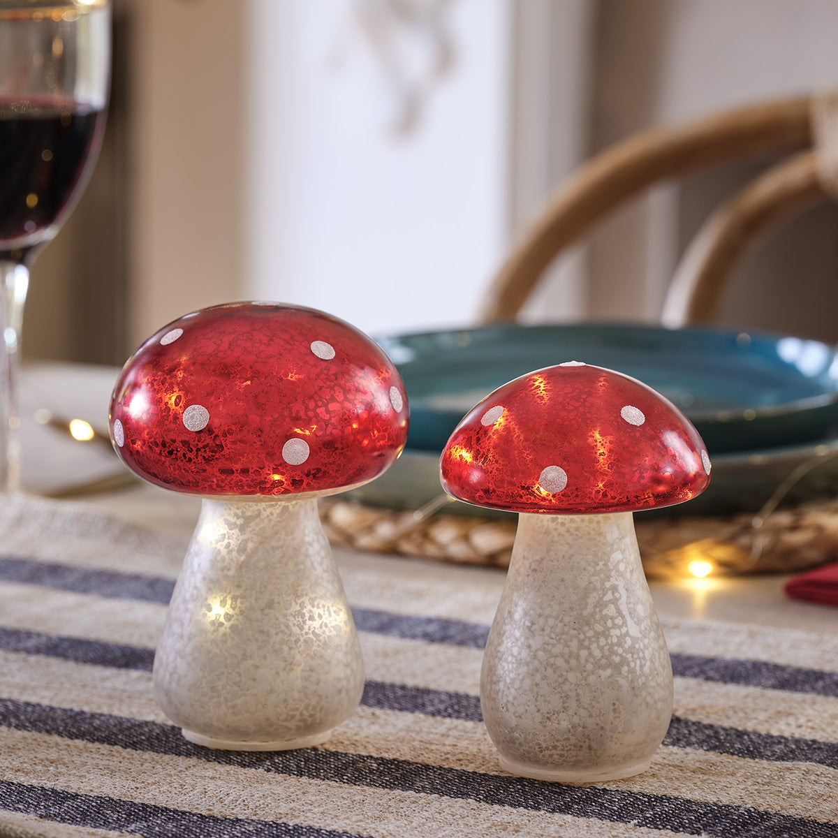 Zwei leuchtende Glas-Fliegenpilze mit roten Kappen und weißen Punkten auf einem Tisch.