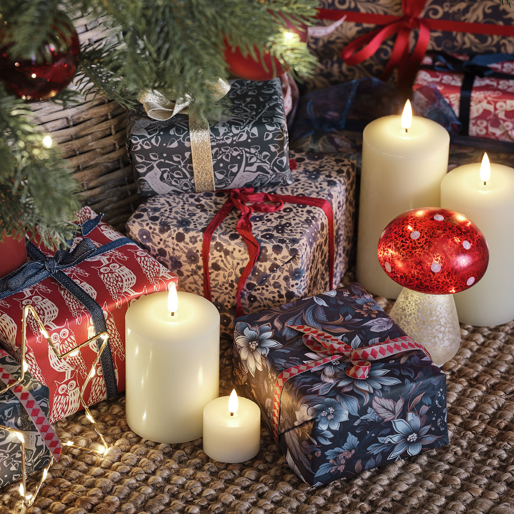 Leuchtender Glas-Fliegenpilz zwischen Kerzen und Weihnachtsgeschenken unter einem Tannenbaum.
