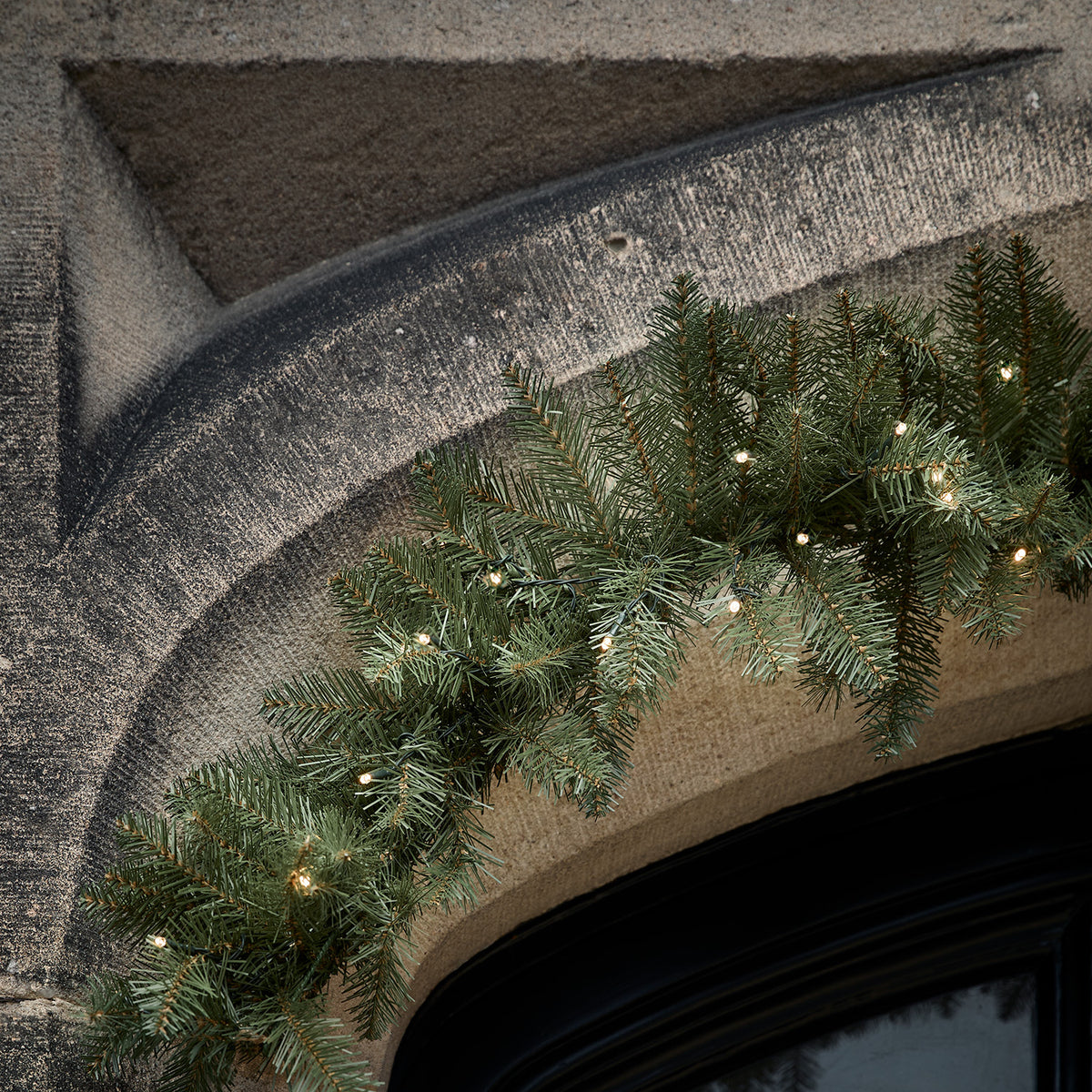 Beleuchtete Weihnachtsgirlande mit Tannenzweigen an einem Steinbogen