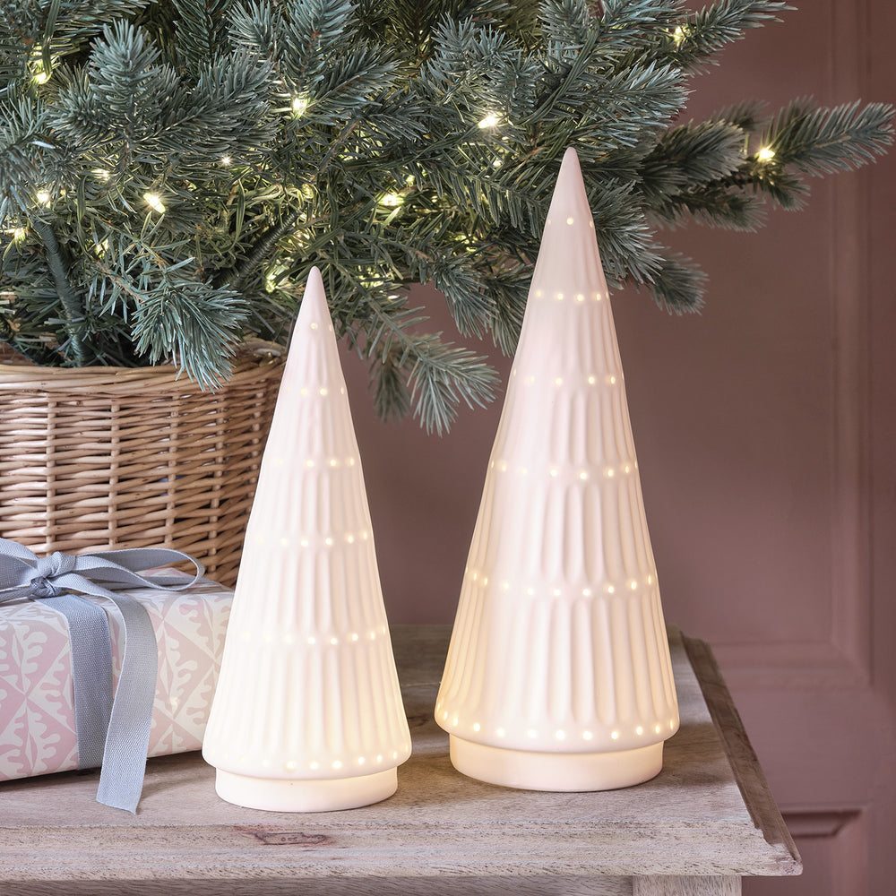 Zwei weiße LED Keramik Weihnachtsbäume vor einem Tannenzweig mit Lichterkette