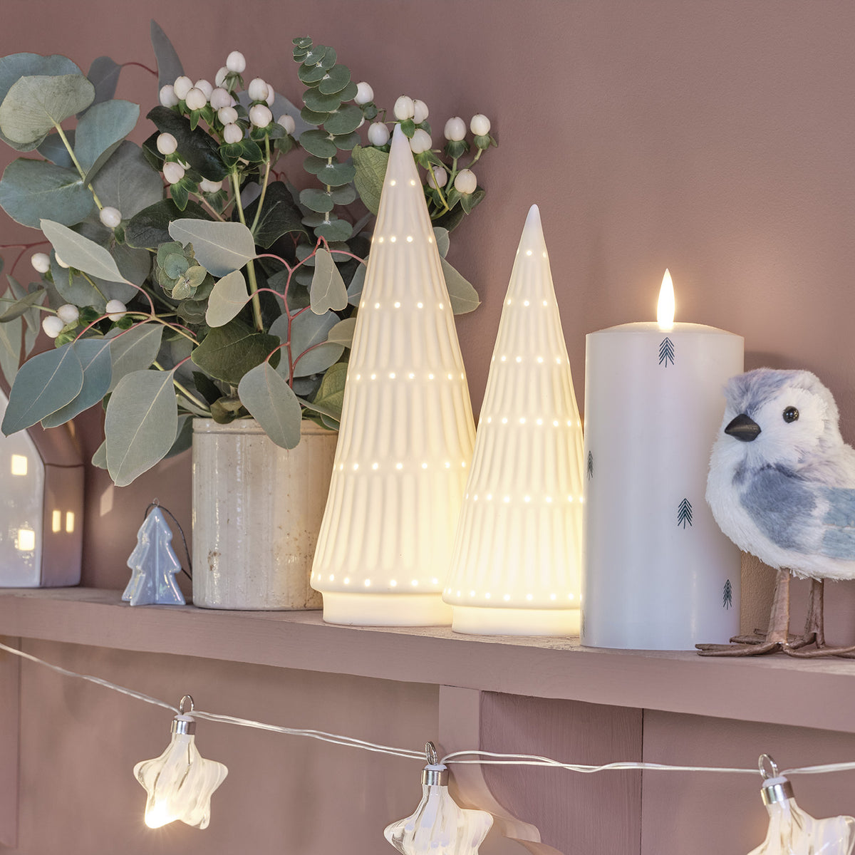 Beleuchtete LED Keramik Weihnachtsbäume neben Kerze und Vogel-Deko auf Regal