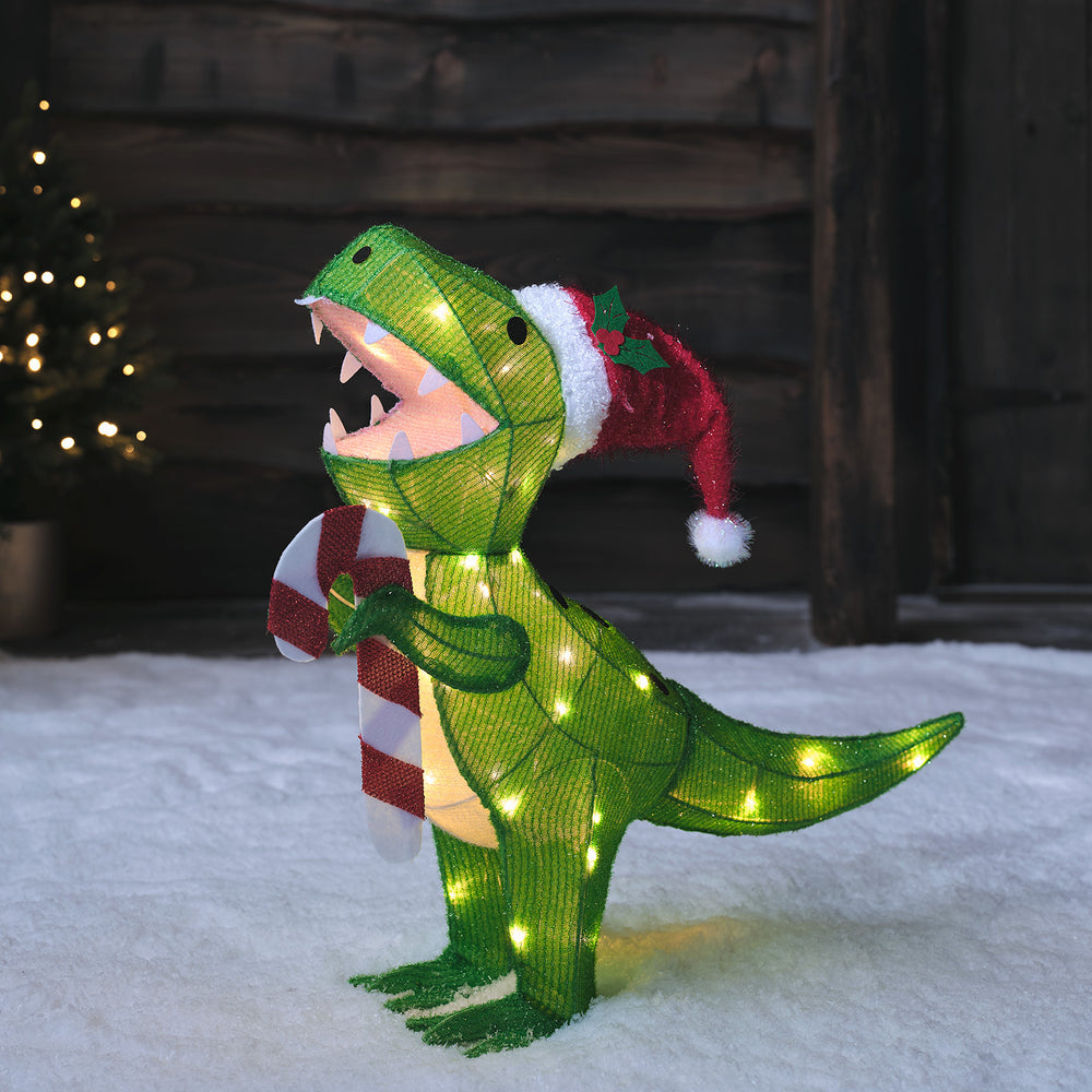 Beleuchtete grüne Dinosaurier-Weihnachtsfigur mit roter Mütze und Zuckerstange im Schnee