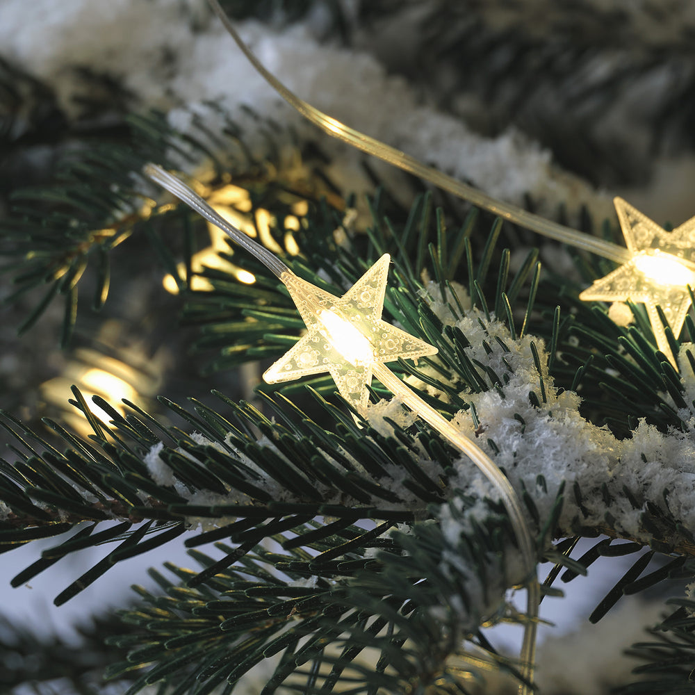 Nahaufnahme eines leuchtenden LED Sterns der Lichterkette auf schneebedecktem Tannenzweig