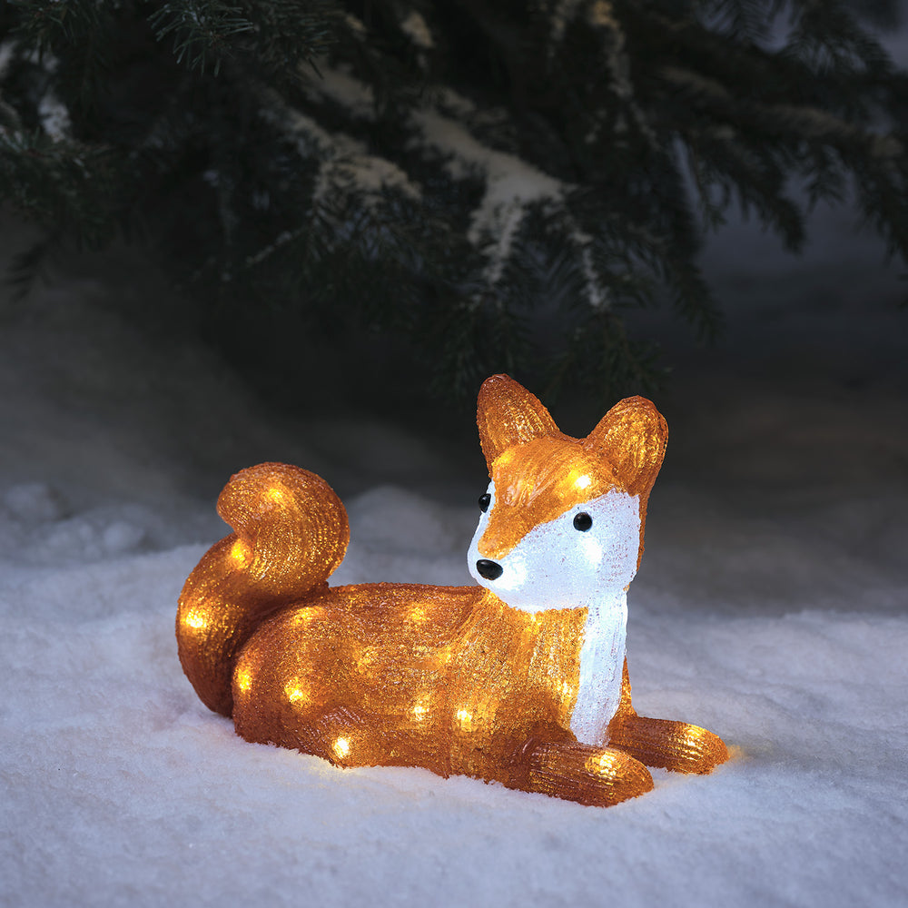 Leuchtende LED Acrylfigur eines liegenden Fuchses im Schnee vor dunklem Tannenzweig