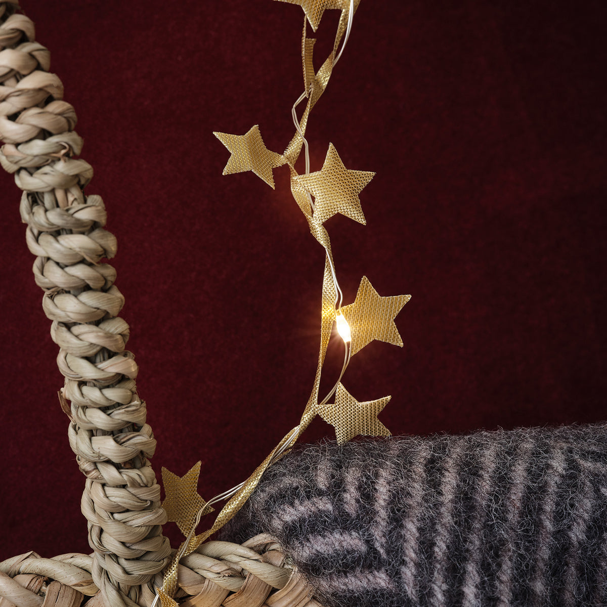 Goldene Stern-Girlande mit LEDs an geflochtenem Korb vor rotem Hintergrund