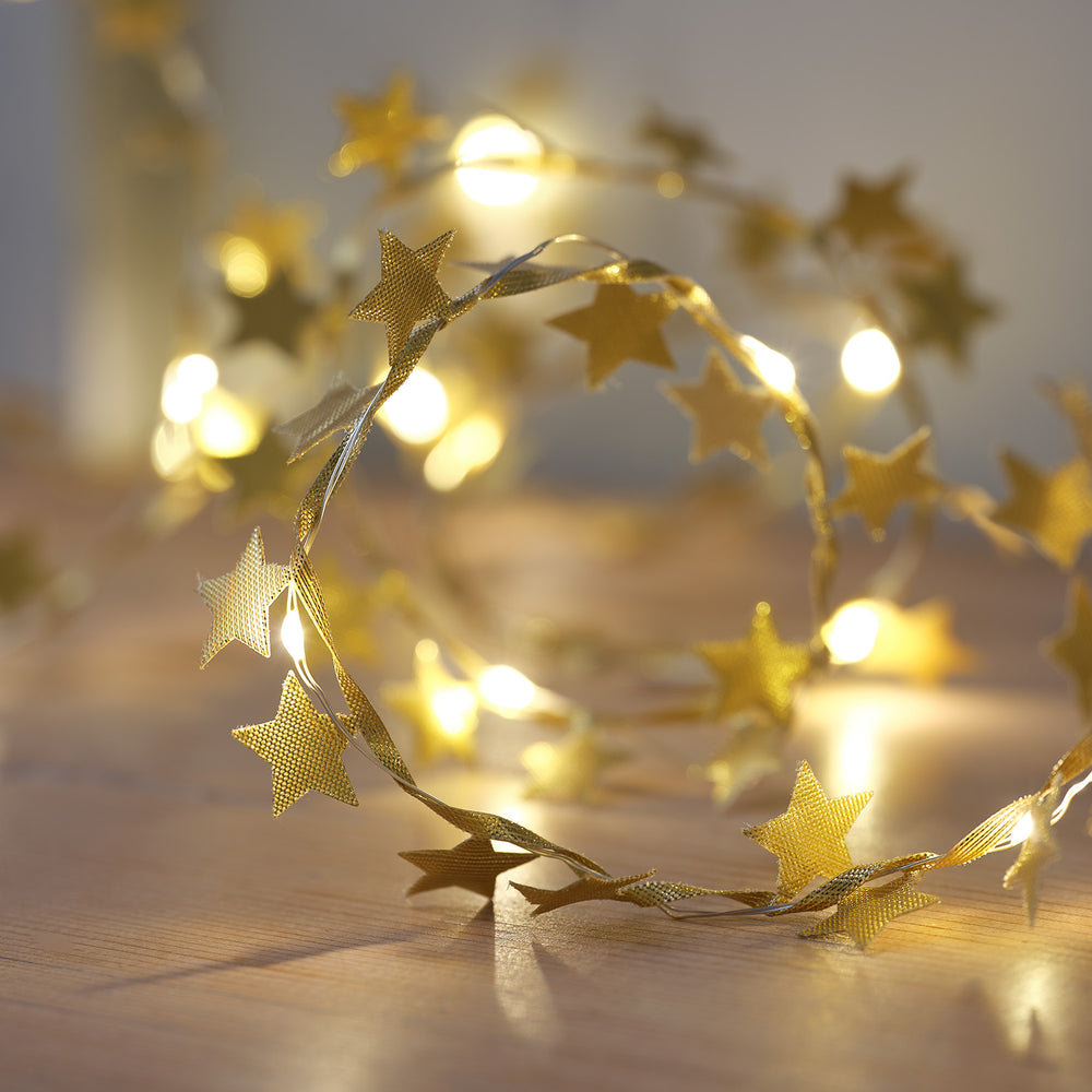 Nahaufnahme goldene Stoffsterne mit Micro LEDs auf hellem Holztisch