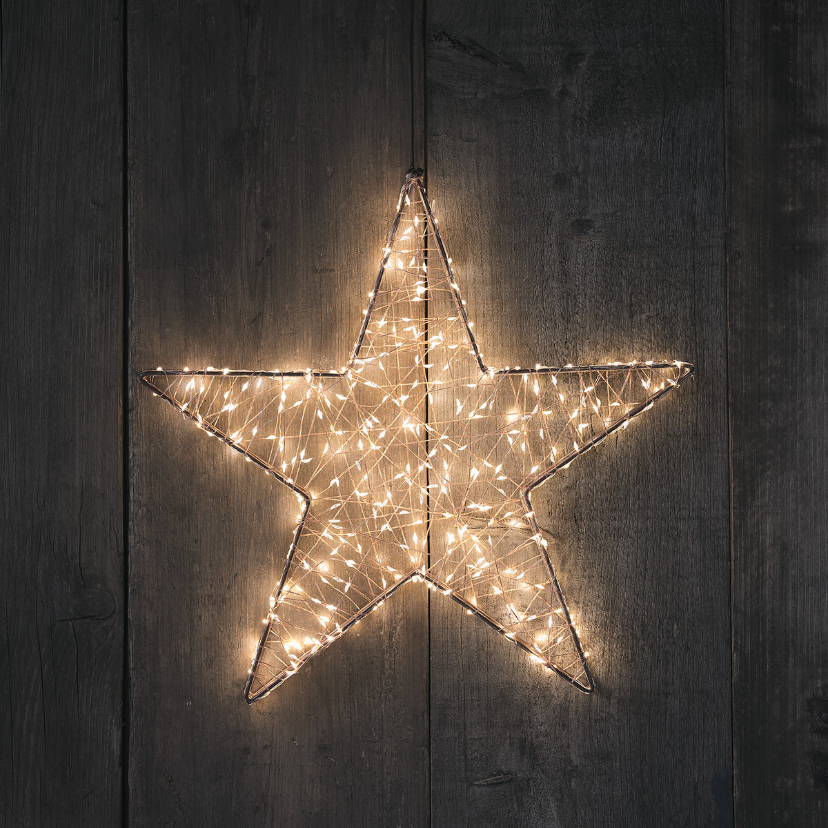 Nahaufnahme eines kupferfarbenen Sterns mit warmweißen Micro-LEDs an Holzwand