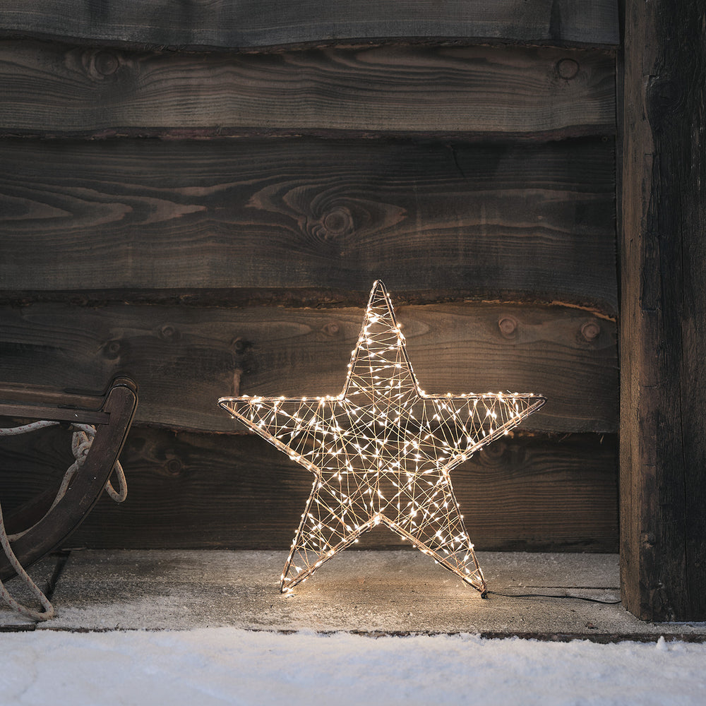 Leuchtender kupferfarbener Stern mit Micro-LEDs vor dunkler Holzwand im Schnee