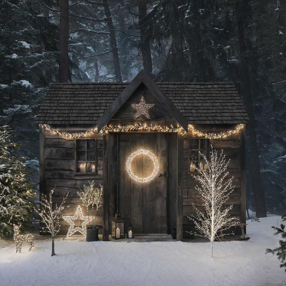 Weihnachtlich dekorierte Holzhütte mit beleuchtetem Stern und Lichterketten im Winterwald
