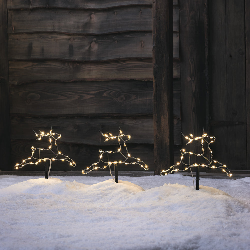 Drei beleuchtete LED-Rentier-Silhouetten im Schnee vor einer Holzwand