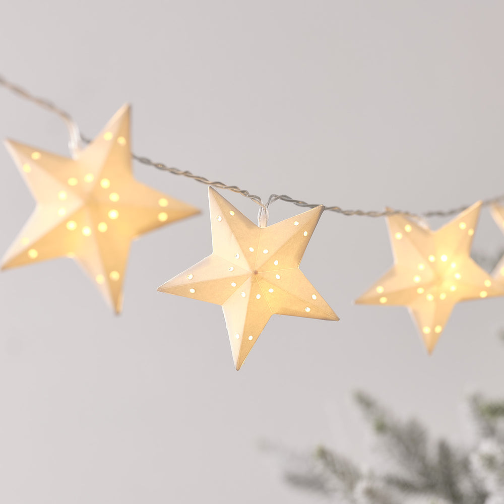 Nahaufnahme einer LED-Lichterkette mit warmweißen Papiersternen und filigranen Lochmustern