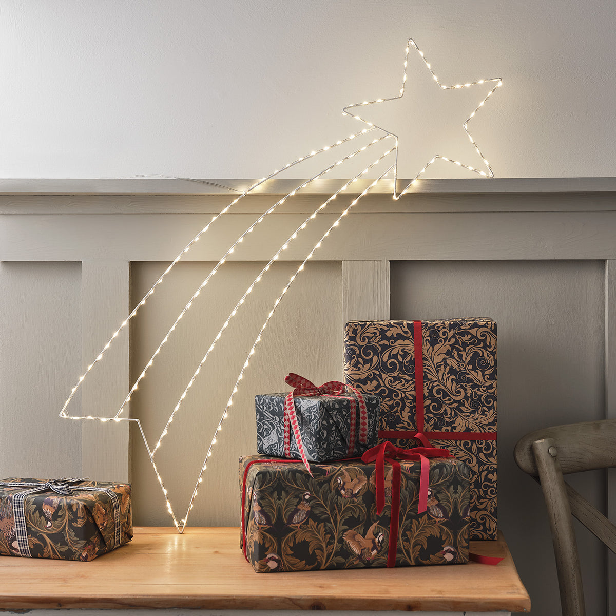 Leuchtende Micro LED Sternschnuppe über Holztisch mit Weihnachtsgeschenken
