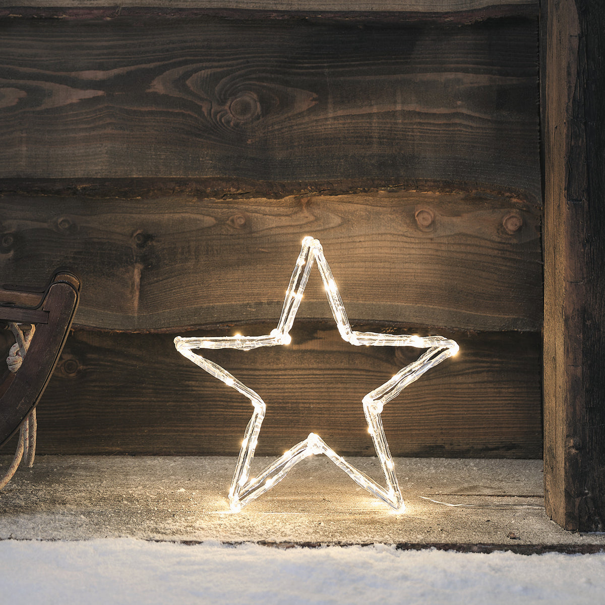 Leuchtender Acrylstern mit warmweißen LEDs vor dunklem Holz im Schnee