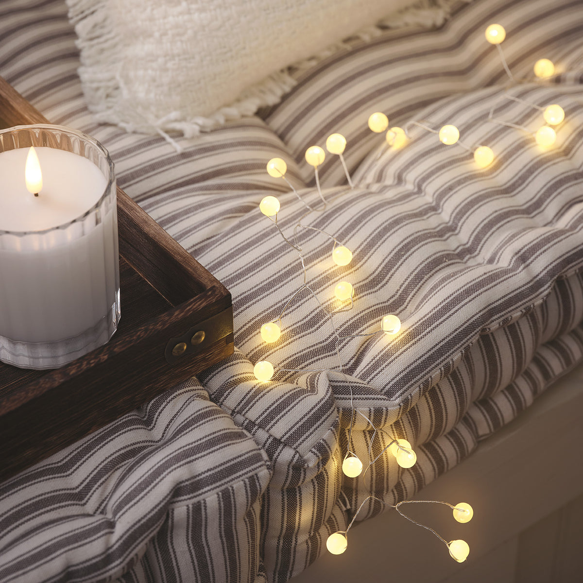 Warmweiße Micro LED Lichterkette mit Kugeln auf gestreiftem Kissen neben Kerze