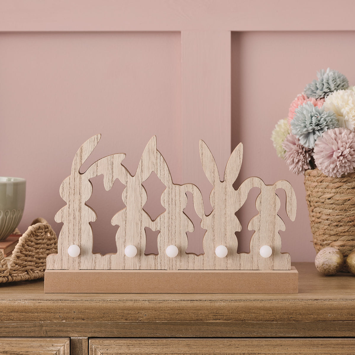 Holz-Osterhasen-Deko mit fünf weißen LED-Kugeln auf Holzsockel vor rosa Wand