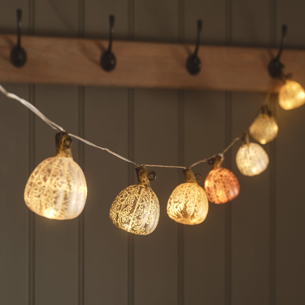 LED Lichterkette mit acht leuchtenden Kürbissen aus Glas vor Holzhaken an Wand