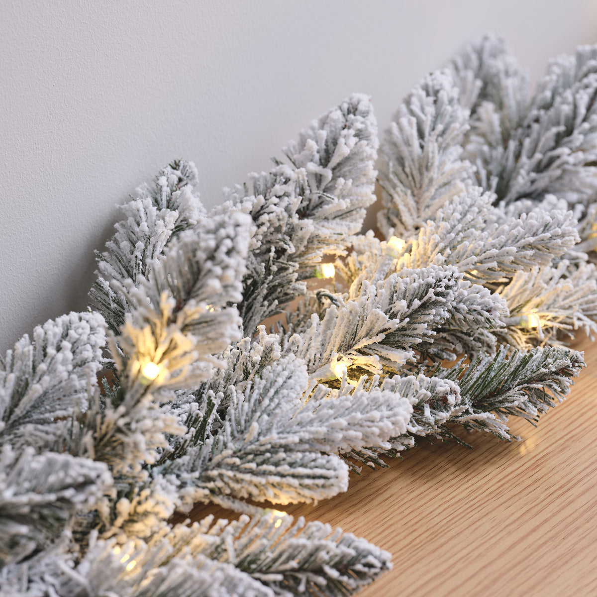 Nahaufnahme verschneiter Tannenzweige mit warmweißen LED-Lichtern auf Holzfläche