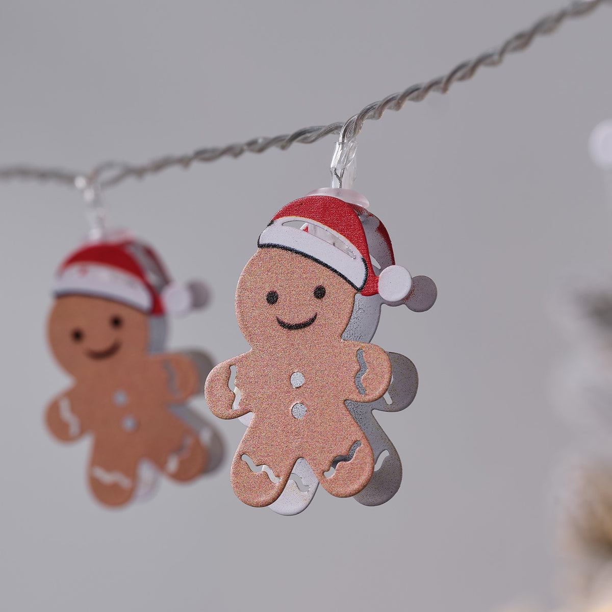 Nahaufnahme eines einzelnen Lebkuchenmännchens mit Weihnachtsmütze an LED-Lichterkette
