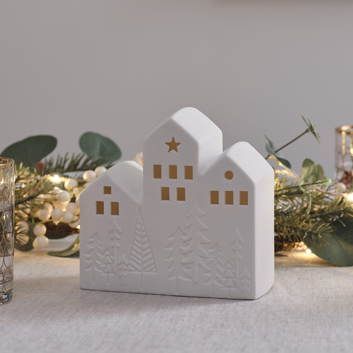 Keramik-Weihnachtshaus mit beleuchteten Fenstern vor Weihnachtsdeko auf Tisch