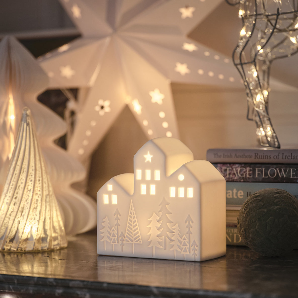 Beleuchtetes Keramikhäuschen mit Sternen und Tannenbaum-Motiv in festlicher Dekoration