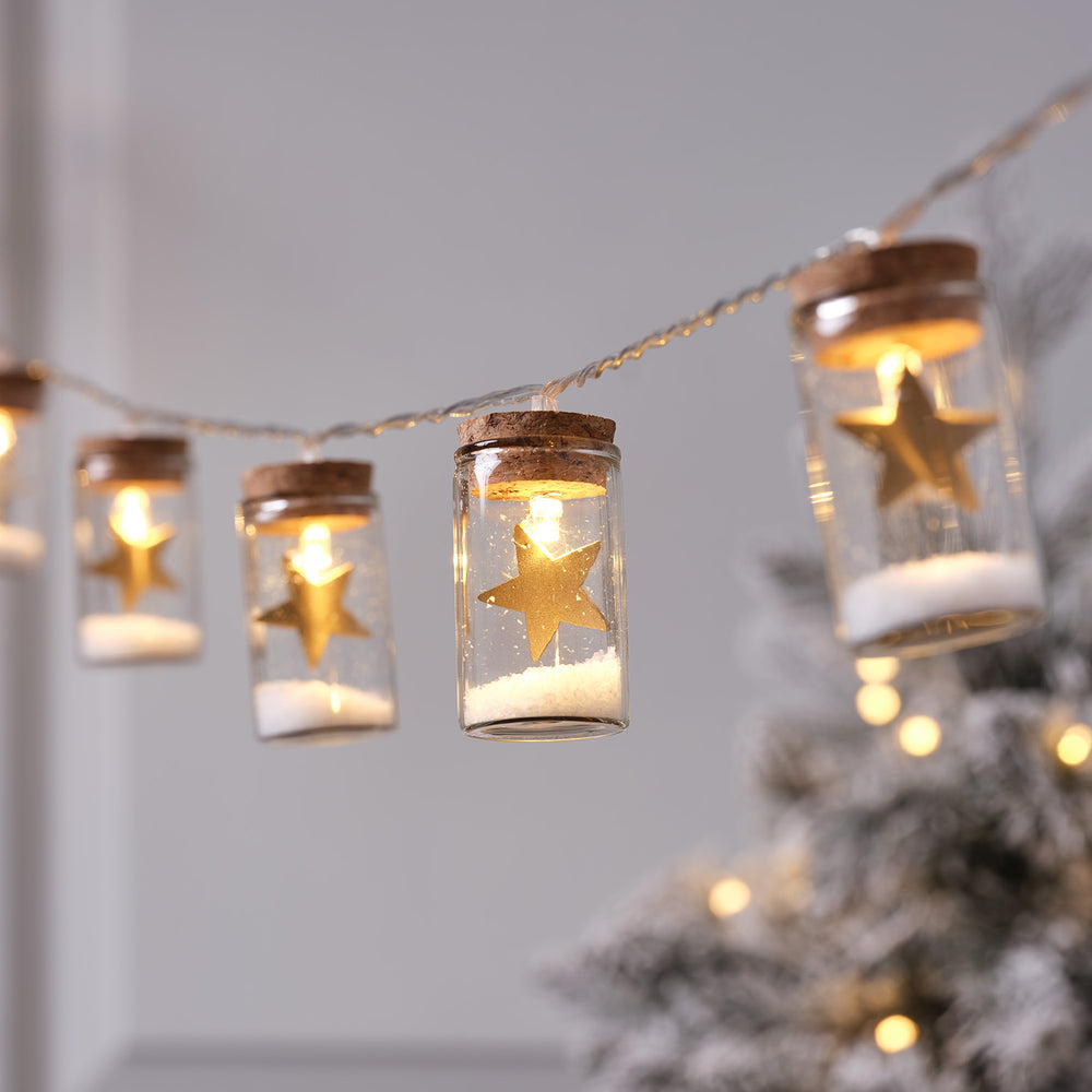 Nahaufnahme der LED-Lichterkette mit goldenen Sternen in Glasfläschchen vor grauem Hintergrund
