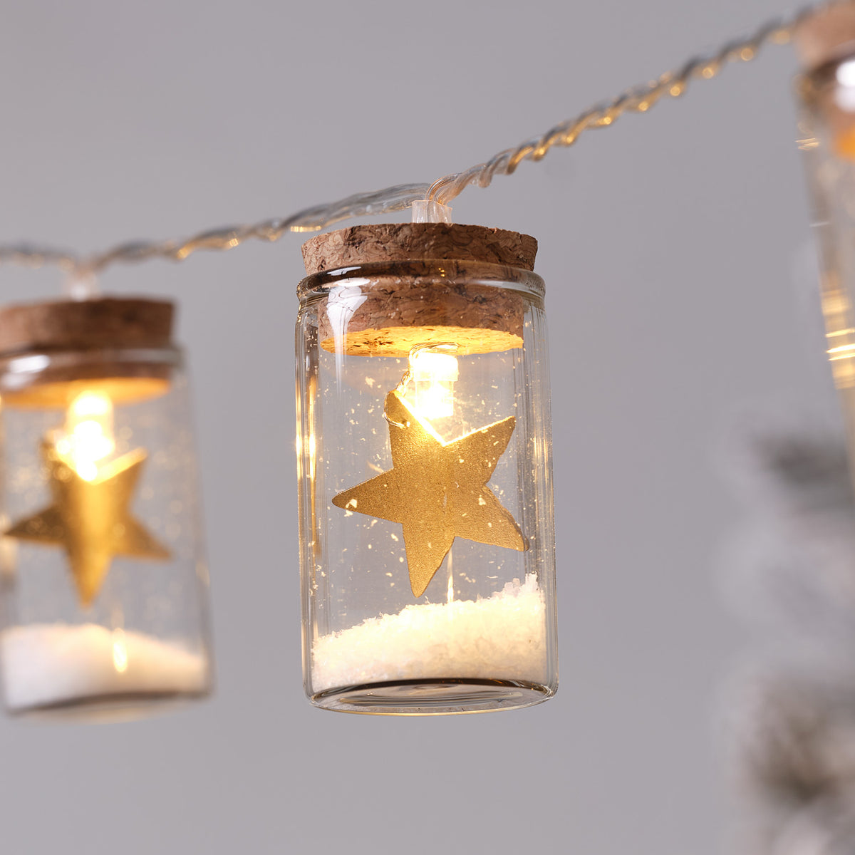 Detailaufnahme eines beleuchteten Glasfläschchens mit goldenem Stern und Kunstschnee