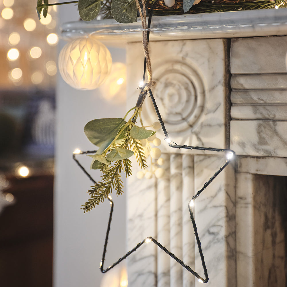 Nahaufnahme eines schwarzen LED-Sterns mit warmweißen Lichtern und künstlichem Wintergrün