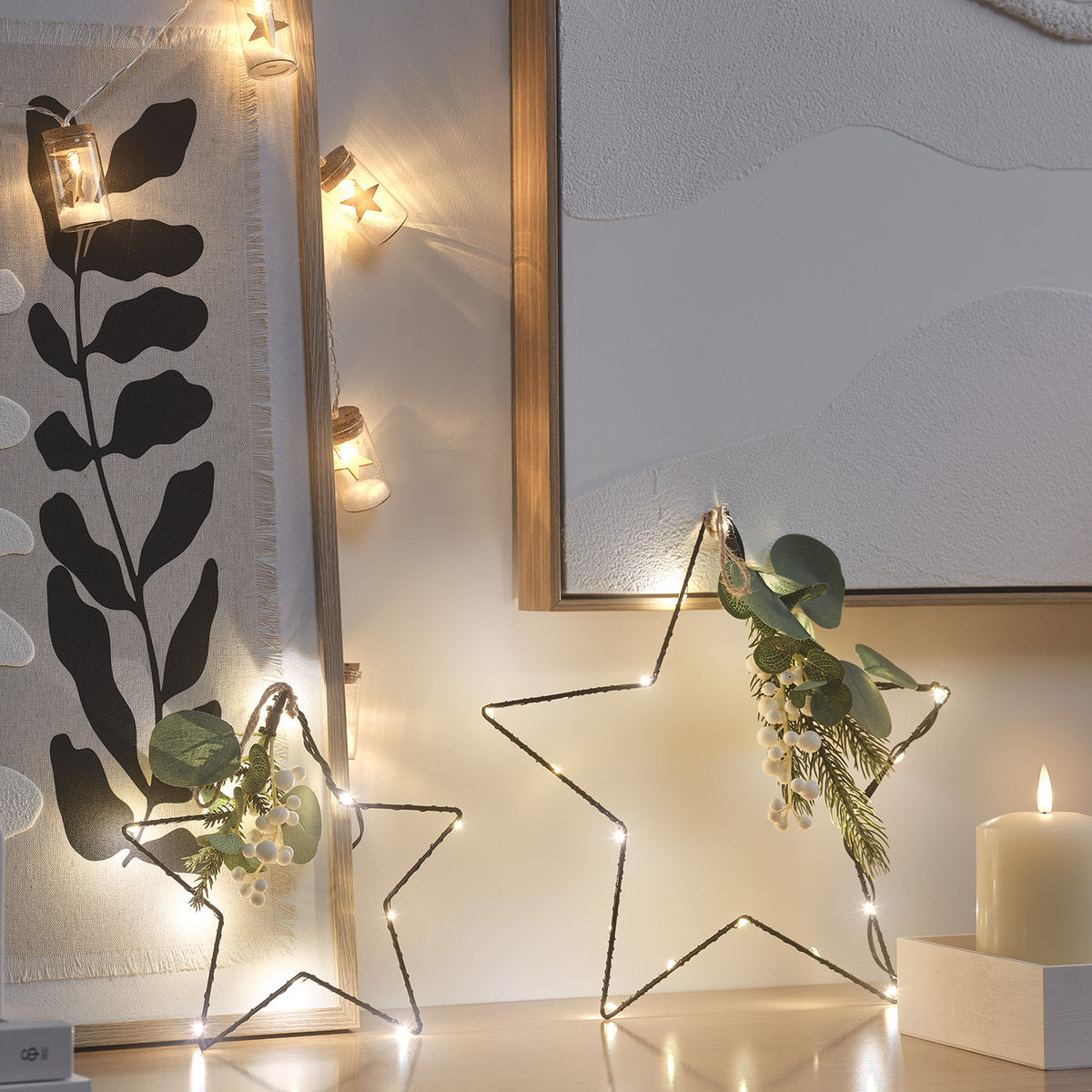 Beleuchtete LED-Sterne mit künstlichem Wintergrün stehen vor einem Spiegel und einer Kerze