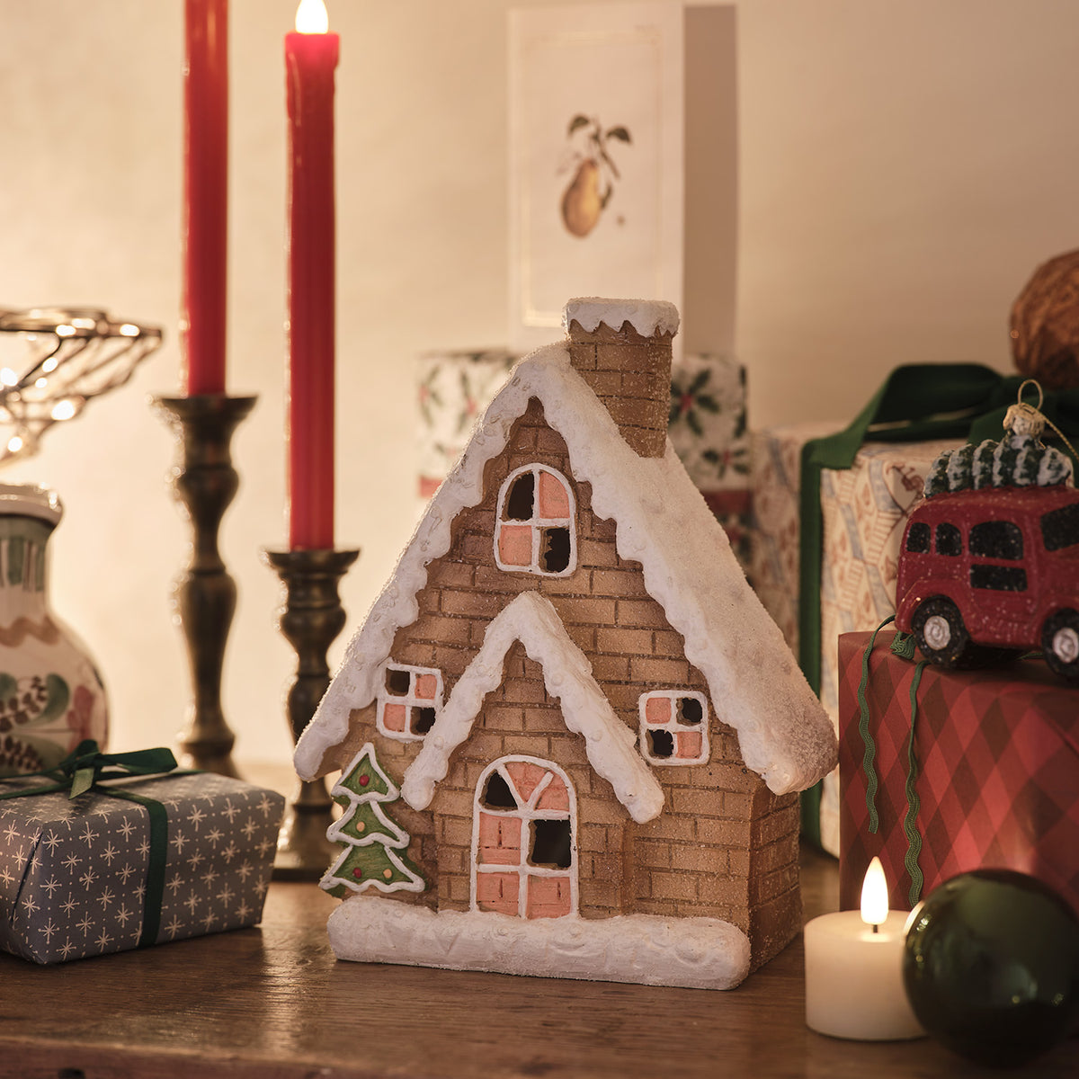 Lebkuchenhaus ohne Beleuchtung, Keramik mit Schnee und Weihnachtsbaum, umgeben von Kerzen und Geschenken