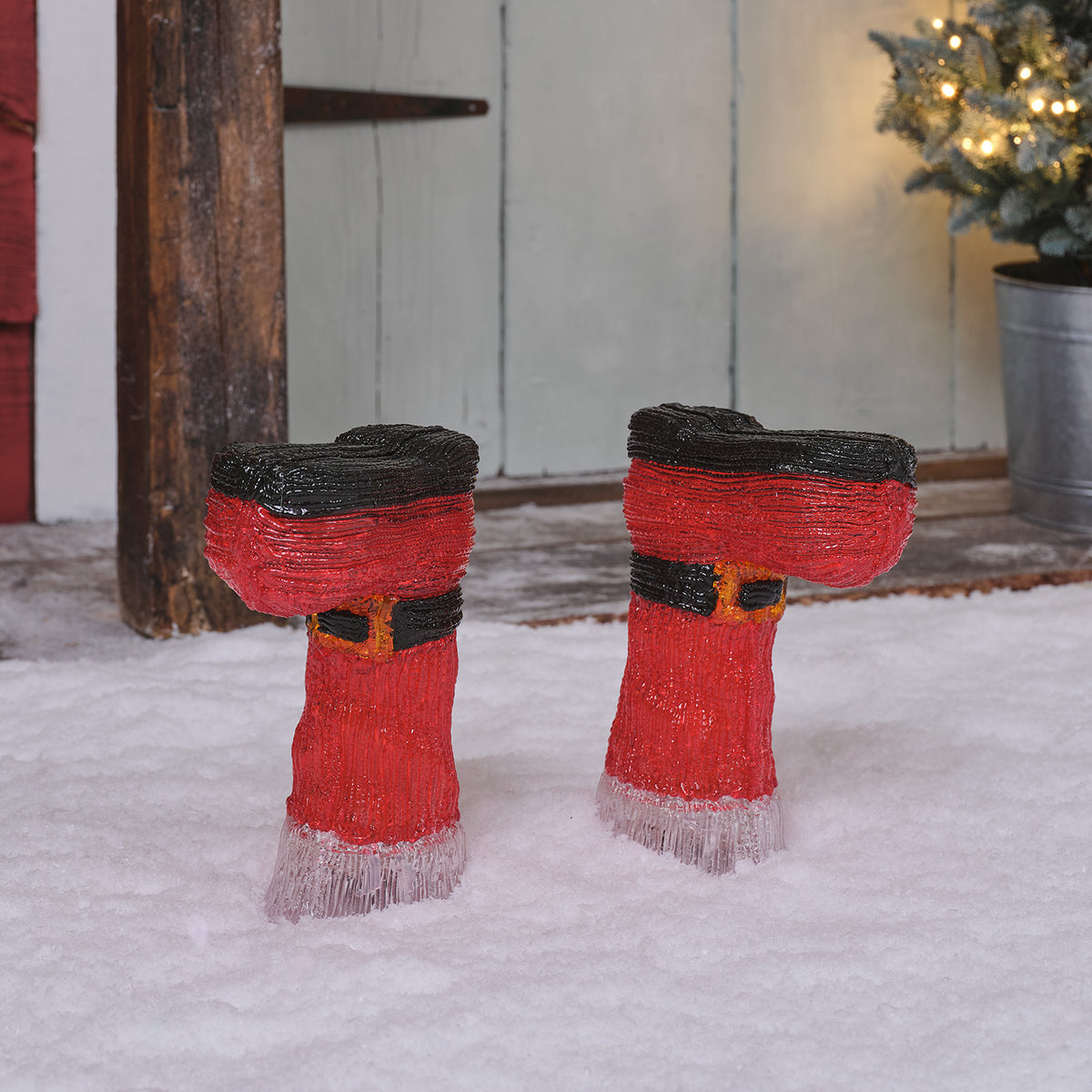 Rote Weihnachtsstiefel aus Acryl ohne Beleuchtung stehen im Schnee vor einer Holzwand