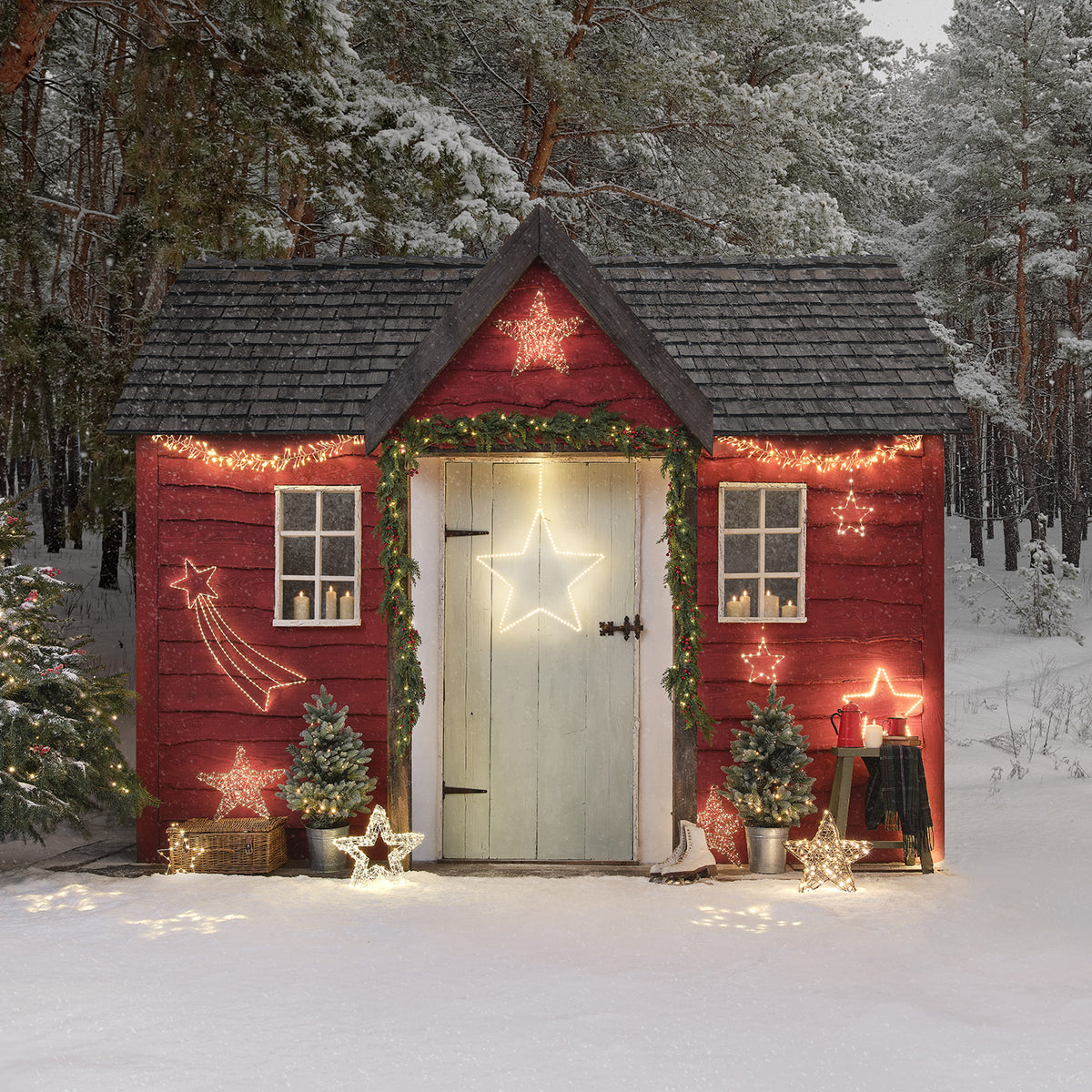 Weihnachtlich geschmücktes rotes Gartenhaus mit leuchtenden LED-Sternen an Fassade und Tür