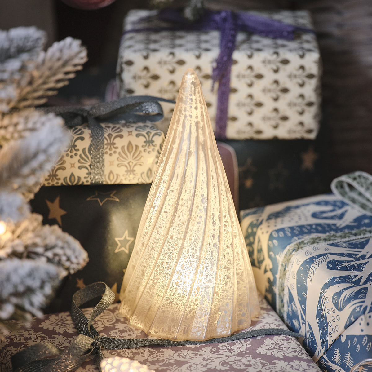 Leuchtender LED-Weihnachtsbaum aus gerilltem Glas mit Quecksilber-Effekt vor festlich verpackten Geschenken
